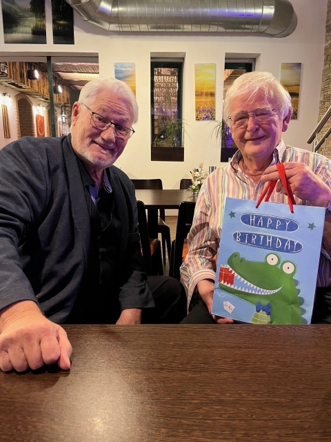 Links Prof. Dr. Peter Stippl, rechts Norbert Neuretter. Neuretter hält ein Geschenkssackerl in der Hand, auf welchem ein Krokodil und der Schriftzug "Happy Birthday" abgebildet ist.