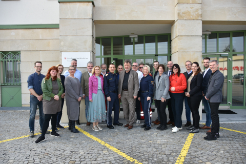 Gruppe von etwa 20 Personen, darunter mehrere uniformierte Polizist:innen, vor dem Eingang der Landespolizeidirektion. Sie stehen nebeneinander für ein gemeinsames Foto im Außenbereich eines Gebäudes mit grünen Türen.