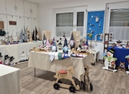 Ausstellung weihnachtlicher Bastel- und Holzdekorationen in einem hellen Raum, darunter handgemachte Wichtel, Adventkalender, Holzschneemänner, bemalte Holzbäume, kleine Geschenkartikel sowie farbenfrohe Dekorationen auf mehreren Tischen.