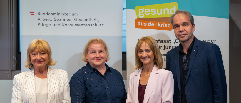 Vier Personen stehen bei einer Presseveranstaltung vor einem Banner des Bundesministeriums für Arbeit, Soziales, Gesundheit, Pflege und Konsumentenschutz sowie einem „gesund aus der krise“-Roll-up und blicken in die Kamera.